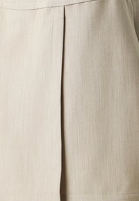 Beige folderet stoff med en glatt tekstur og subtile linjemønstre. Designet har pent syede sømmer.