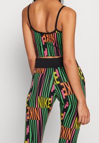 Kolorowy zestaw crop topu i legginsów z czarnym tłem, pionowymi paskami w kolorach zielonym, różowym i żółtym, z logo "NIKE" rozmieszczonymi w całym wzorze.