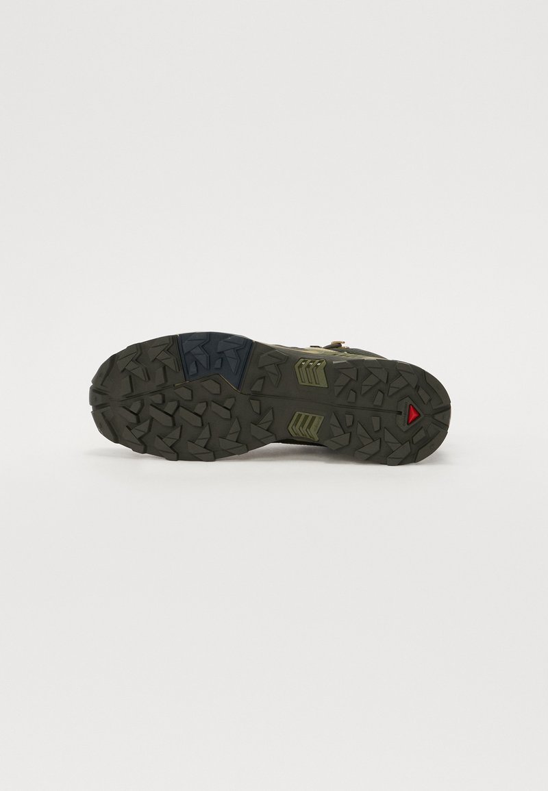 Green trail shoe sole featuring a rugged tread design with multi-directional grips, accentuated by a blue and red triangular insert.