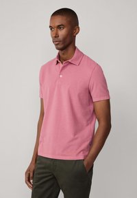 Różowa koszulka polo o slim fit, z krótkim rękawem i wywijanym kołnierzykiem. Posiada zapięcie na guziki z przodu oraz małe logo z boku. Gładki materiał bawełniany.