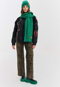 Czarna kurtka puchowa z kwiatowymi akcentami, zestawiona z zielonym szalikiem i czapką, spodniami w panterkę oraz masywnymi zielonymi butami na platformie.