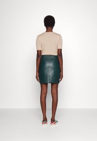 Haut marron à manches courtes associé à une mini-jupe en cuir verte. Les baskets présentent un design multicolore. Fond blanc uni.