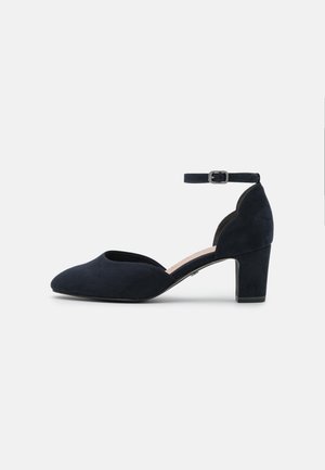 Navy suede pump with a rounded toe, cut-out sides, and a mid-height block heel. An ankle strap features a square buckle for fastening.