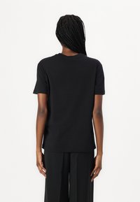 Sort bomulds T-shirt med korte ærmer og rund hals, der har en afslappet pasform og glat tekstur. Båret med løstsiddende sorte bukser.