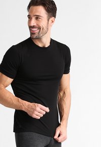 Svart kortermet treningst-skjorte laget av stretchy materiale, tettsittende design, rund hals, og glatt tekstur. Minimal merkevare på bunnen.