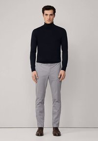 Marinblå polotröja med åtsittande silhuett, kombinerad med ljusgrå byxor och bruna läderskor. Enkel design med slät tygstruktur.