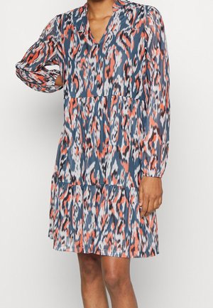 Femme portant une robe à manches longues, longueur genou, avec un motif abstrait d'animaux en bleu, orange, blanc et noir.