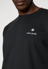 Black cotton t-shirt featuring a crew neck, short sleeves, and a white logo with an asterisk and the words "snow peak" on the chest.