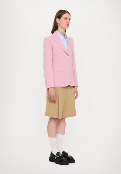 Pink tailored blazer, light blue shirt, beige shorts, black loafers with buckle, and white knee-high socks. Flat, smooth textures.