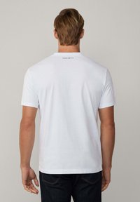 Camiseta de algodón blanca con mangas cortas, escote redondo y un sutil logotipo negro "HACKETT" en la parte superior de la espalda.