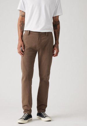 Brown cotton pants with a classic straight leg fit, belt loops, and front pockets, paired with black sneakers and a white t-shirt.