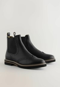 Mustad nahast Chelsea saapad on kaunistatud brogue-detailidega, neil on elastsed külgpaneelid ja kihiline konts kummist tallaga, mis tagab haarduvuse.