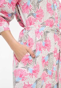 Tunic in tessuto leggero con motivo floreale, dettagli in rosa, blu e grigio. Presenta una vita con lacci, chiusura a bottoni e tasche laterali.