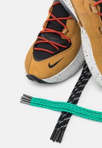 Bruna mocka sneakers med svart mesh och röda snören. Vitprickig sula. Inkluderar teal- och svartmönstrade skosnören.