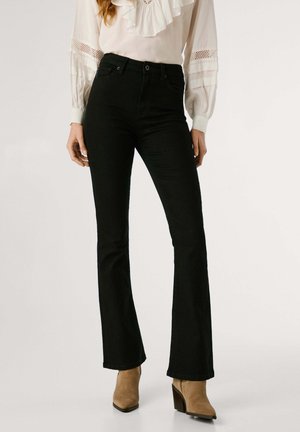 Zwarte flare jeans van katoen, met een hoge taille en een subtiele stretch. Gekleed met een witte blouse en tan kleurige met hakken enkellaarsjes.