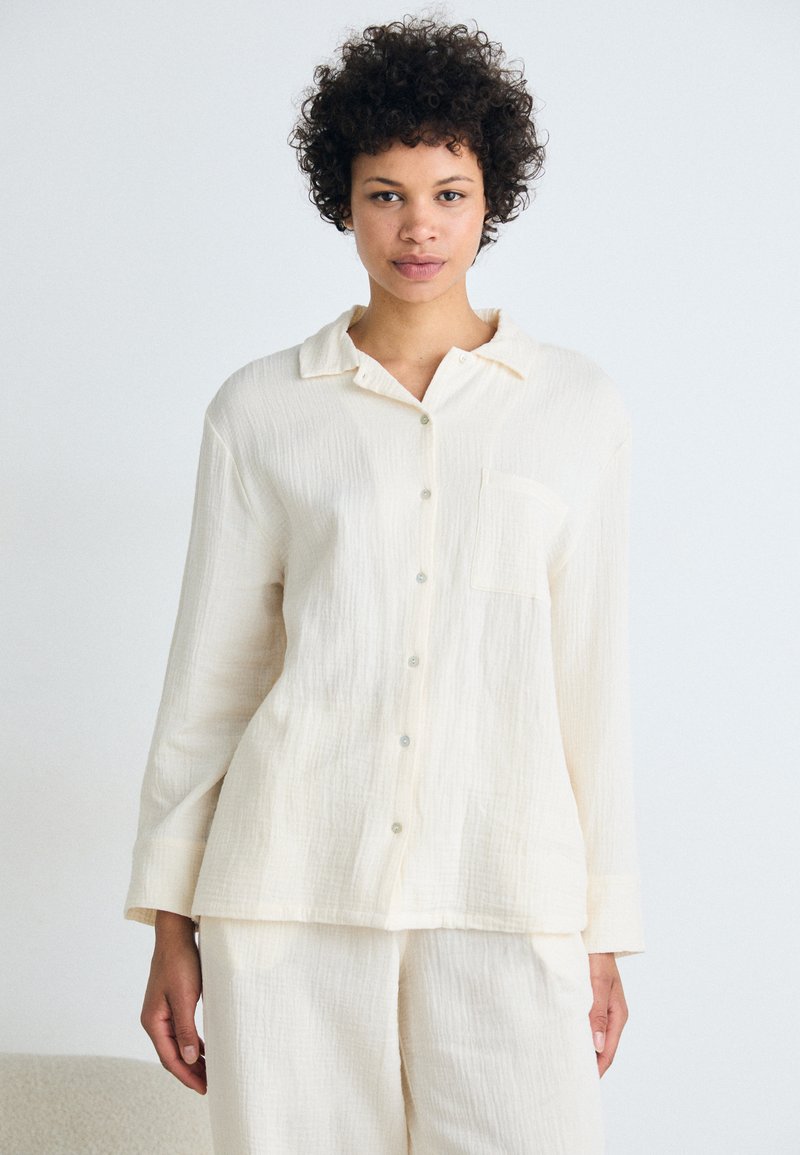 Off-white teksturert skjorte med lange ermer og krage, som har en brystlomme og en avslappet passform.