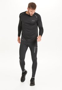 Svart långärmad träningströja med reflexdetaljer, kombinerad med matchande åtsittande leggings, båda gjorda av andningsbart material.