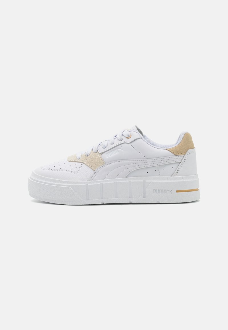 Baskets blanches avec des accents en suedine beige, tige perforée, semelle épaisse et texturée, et logo de la marque sur le côté et au talon. Design à bout rond.