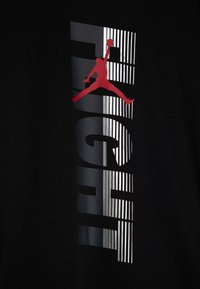 Svart t-shirt med en vertikal grafik där "FLIGHT" står i fetstil, en röd silhuett av en basketspelare och randiga detaljer.