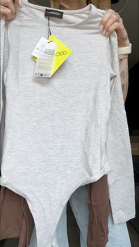 Body grigio chiaro a maniche lunghe con scollatura rotonda, realizzato in tessuto morbido. Etichette attaccate; presenta un design a perizoma.