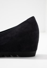 Chaussure compensée en suède noir avec un bout arrondi et une surface texturée. Présente une semelle en caoutchouc lisse avec un motif en zigzag pour une meilleure accroche.