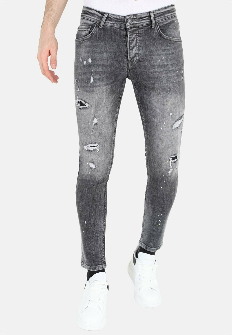 Slim-fit, grijze spijkerbroek van denim met versleten details, scheuren en spetterpatronen; gecombineerd met witte sneakers.