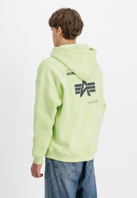 Felpa verde lime con cappuccio regolabile, caratterizzata da un grande logo nero sul retro e polsini e orlo a costine. Vestibilità comoda con una consistenza morbida.