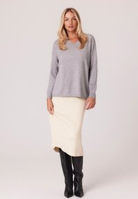Jasnoszara dzianinowa sweter z dekoltem w serek, zestawiony z kremową prążkowaną spódnicą midi i czarnymi wysokimi botkami. Miękka tekstura, luźny krój.