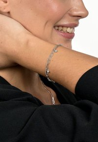 Silver bracelet featuring linked chains with small round accents, set against a black garment, highlighting texture and shine.