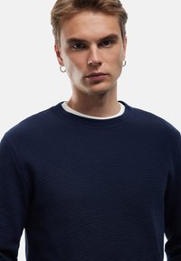 Felpa blu navy con texture, colletto rotondo e colletto interno bianco. Presenta dettagli a coste e una vestibilità rilassata.