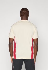 Kortærmet t-shirt i creme med røde sidepaneler. Glat stof, rund halsudskæring og atletisk pasform. Minimal branding på ryggen.