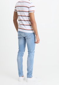 Vit randig t-shirt med blå, orange och röda ränder, tillsammans med ljusblå denimjeans. Har en slim fit och minimalistiska vita sneakers.