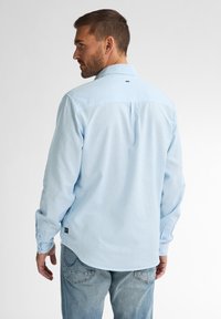 Světle modrá košile s dlouhým rukávem, button-down límcem, jedním zadním skladem a jemným logem blízko výstřihu. Bavlněná tkanina.