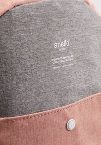 Borsa Anello con parte superiore in tessuto grigio e parte inferiore rosa, caratterizzata da un bottone metallico rotondo e superficie testurizzata. Marchio visibile.