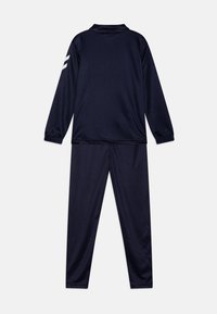 Survêtement marine en tissu lisse ; comporte des manches longues, des poignets élastiques et des accents blancs sur l'épaule gauche. Pantalon avec taille élastique.