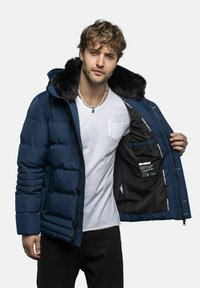 Mørkeblå pufferjakke med h�ætte, der er foret med faux pels. Har knaplukning foran og indvendig lomme. Letvægts, quiltet design med en glat overflade.