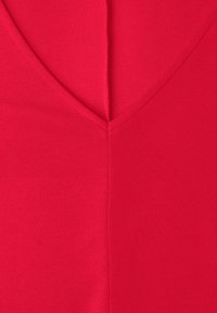 Gros plan sur un tissu rouge avec une couture en forme de V et des bords cousus lisses formant un point central net.