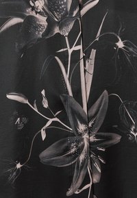 Tissu noir avec un motif floral et de feuilles détaillé de teintes claires, comportant de grandes lys et un petit papillon près du bord gauche.