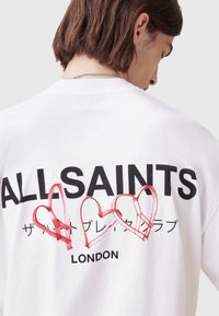 Hvit bomull t-skjorte med svart "ALLSAINTS" logo og røde hjertegrafikker på baksiden, med japansk tekst under og en avslappet passform.