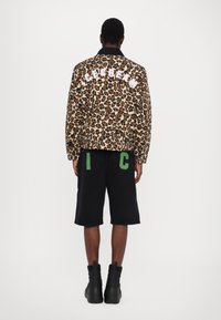 Giacca con stampa leopardata e colletto nero, testo "ICECREAM" sul retro. Pantaloni corti di jeans neri, accenti verdi su tasche con la lettera "I" e "C", stivali neri.
