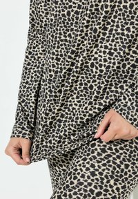 Leopardenmuster-Oberteil und Leggings aus schwarzem und beigem Stoff. Das Oberteil hat lange Ärmel und eine lockere Passform, die eine glatte Textur zur Geltung bringt.