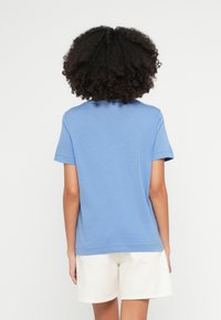 Niebieska bawełniana koszulka z krótkim rękawem, okrągłym dekoltem, luźnym krojem i gładką teksturą, zestawiona z jasnymi szortami.