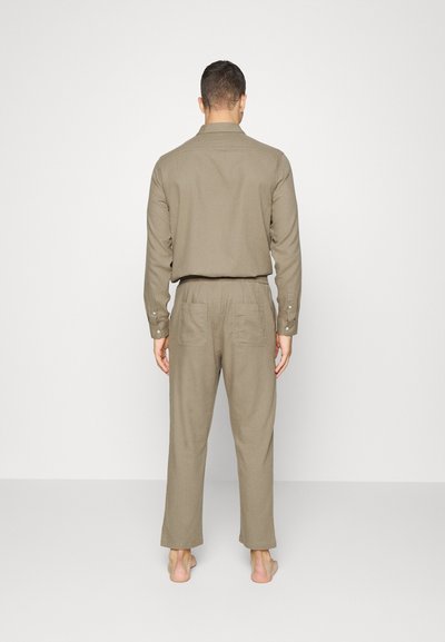 Conjunto de camisa e calças em linho caqui, camisa com botões e colarinho, calças de corte descontraído com bolsos traseiros. Textura suave, cor suavizada.