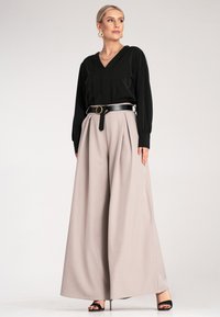 Czarna bluzka z długim rękawem i dekoltem w kształcie litery V, zestawiona z beżowymi spodniami typu wide-leg z wysokim stanem i czarnym paskiem z okrągłą metalową klamrą.