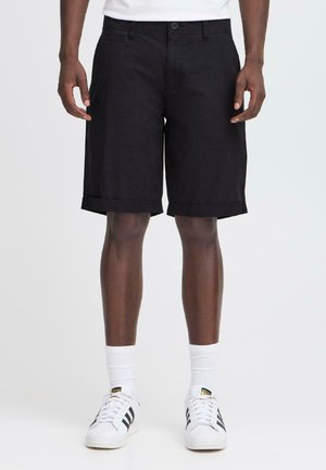 Schwarze Shorts aus Baumwolle, mit geradem Schnitt, umgeschlagenem Saum und seitlichen Taschen. Kombiniert mit weißen Socken und klassischen weißen Sneakern.