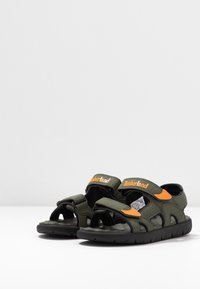 Sandali sintetici verdi con suole nere, con accenti arancioni e cinturini in Velcro. Design aperto con perforazioni per traspirabilità.