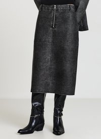 Gonna midi in denim nero con cerniera frontale, cuciture verticali e texture liscia. Abbinata a stivali neri in pelle al ginocchio.