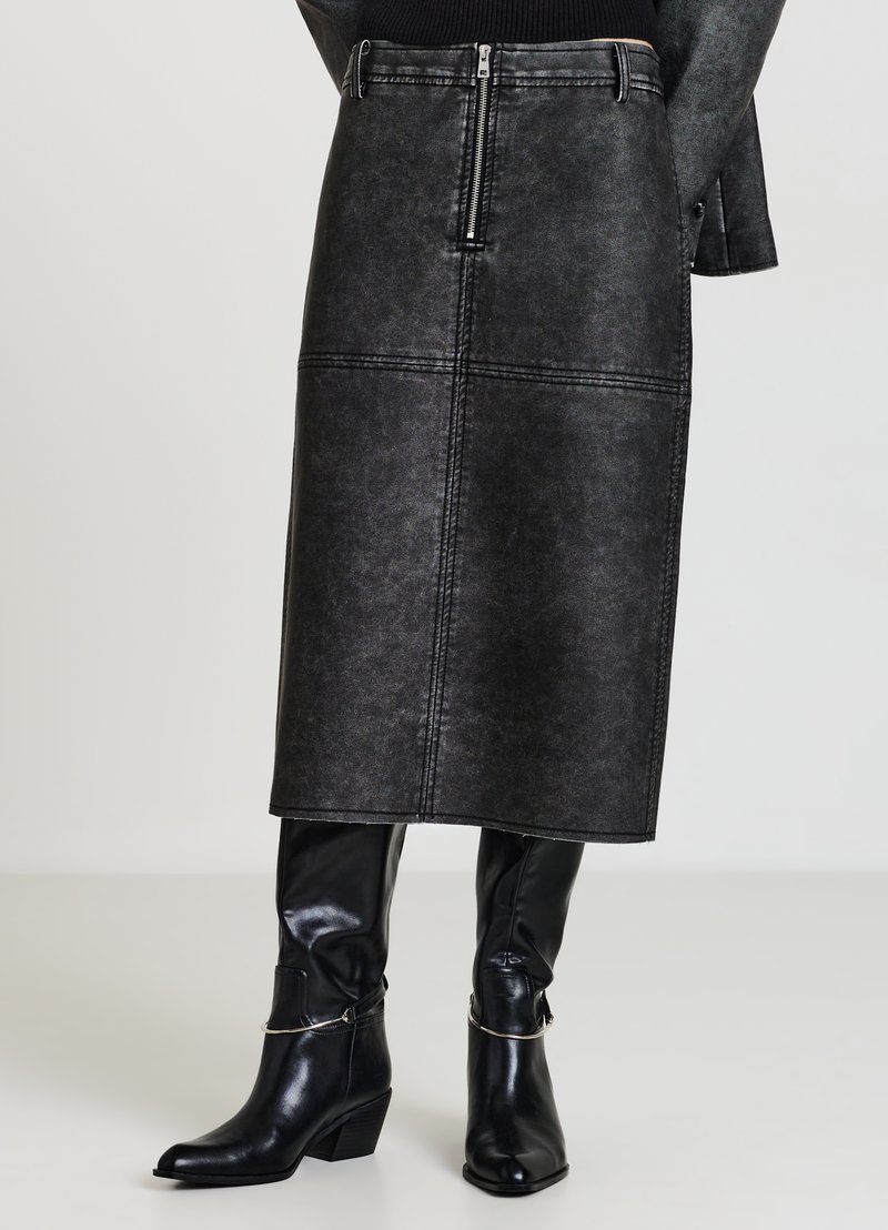 Gonna midi in denim nero con cerniera frontale, cuciture verticali e texture liscia. Abbinata a stivali neri in pelle al ginocchio.