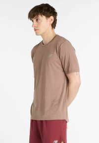 Brown short-sleeve athletic t-shirt with textured fabric and a small gray logo on the chest. Styled with maroon shorts.