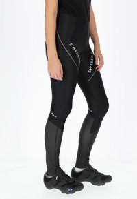 Black cycling leggings with a sleek design, featuring paneling details and reflective accents. Paired with black cycling shoes.